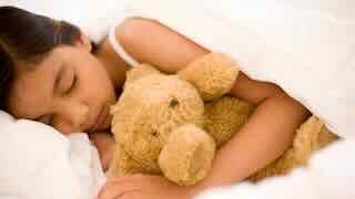 Une jeune fille qui dort avec un ours en peluche.