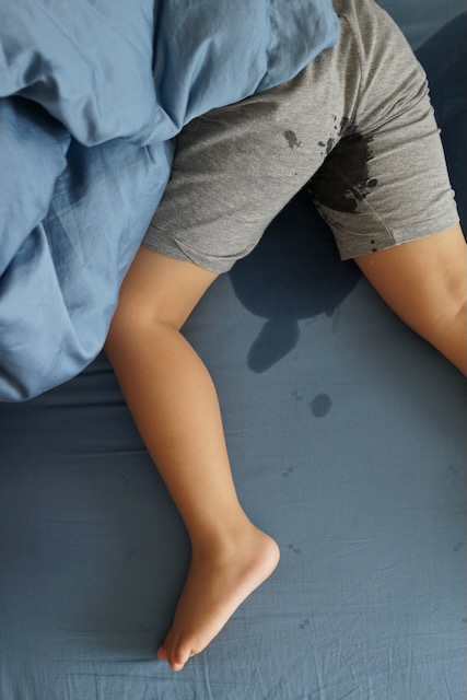 Un enfant allongé sur un lit avec une flaque d’eau dessus.