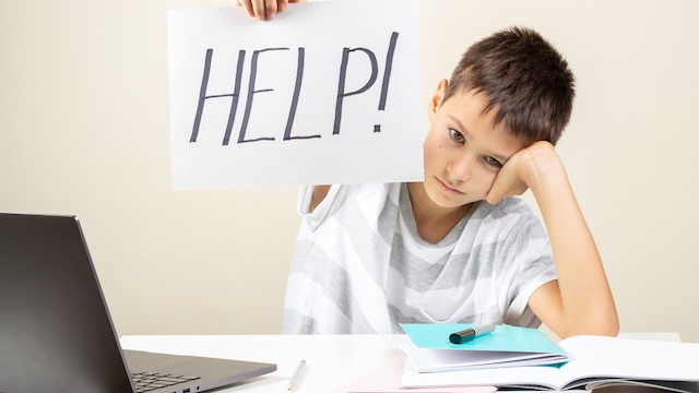 Un garçon dyslexique chez l'adolescent brandissant une pancarte avec le mot aide devant son ordinateur portable, tout en utilisant des stratégies pour DYS.