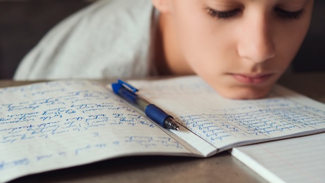 Un adolescent dyslexique écrit dans un cahier avec un stylo, utilise des stratégies et reçoit un soutien adapté aux adolescents dyslexiques.