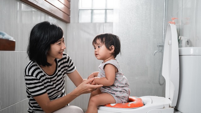 Une femme asiatique avec un bébé assis sur les toilettes.