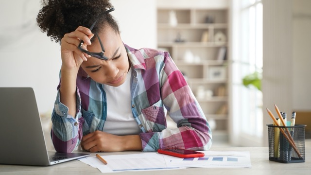 Une jeune femme confrontée au stress de l'orientation scolaire alors qu'elle étudie avec des papiers et un ordinateur portable à un bureau dans une pièce lumineuse.