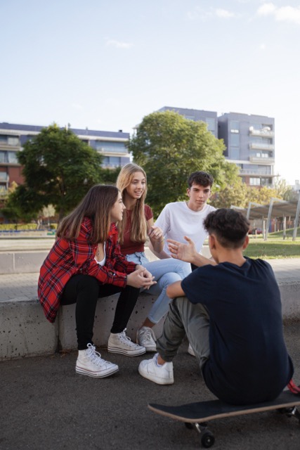 Quatre jeunes adultes discutaient à l’extérieur, assis sur une barrière en béton, l’un d’eux tenant une planche à roulettes.
